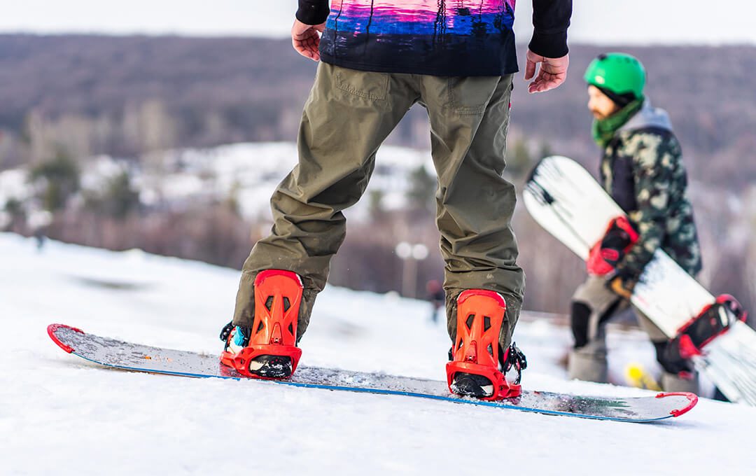 A close-up of a man wearing brown pants riding on a snowboard in a ski park.