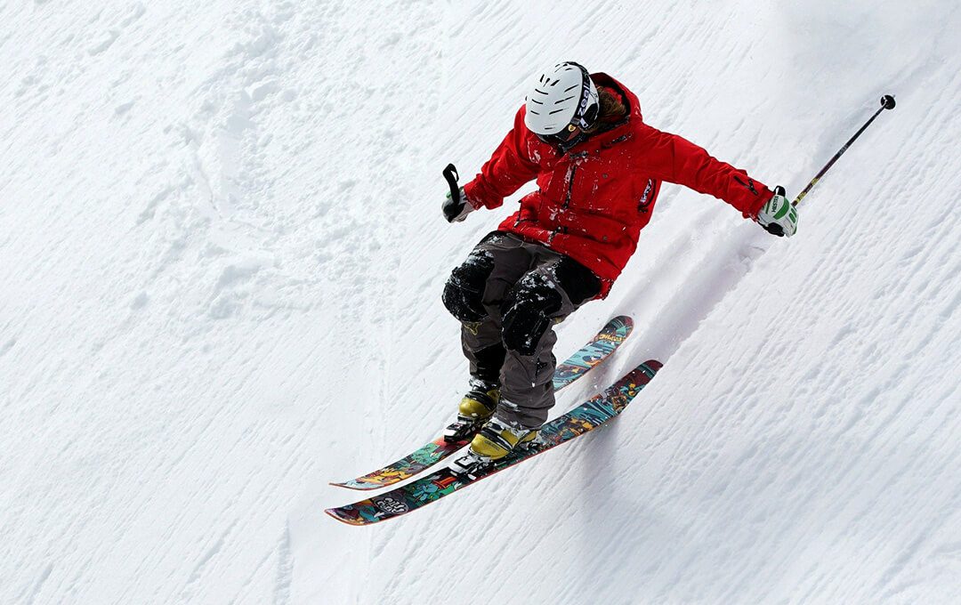 A close-up of a skier wearing a white helmet and a red jacket riding on a ski sliding down a mountain slope.