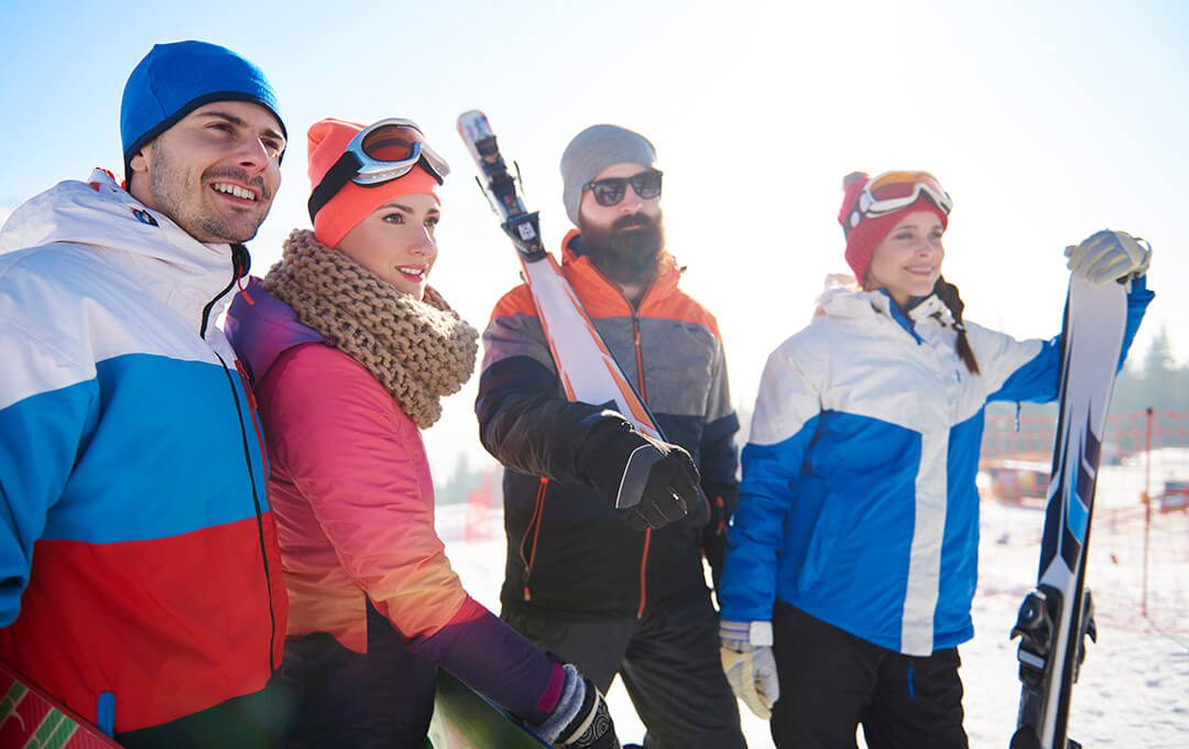 A close-up of four people wearing ski outer jackets holding a ski board on a ski park against a bright blue sky in the background