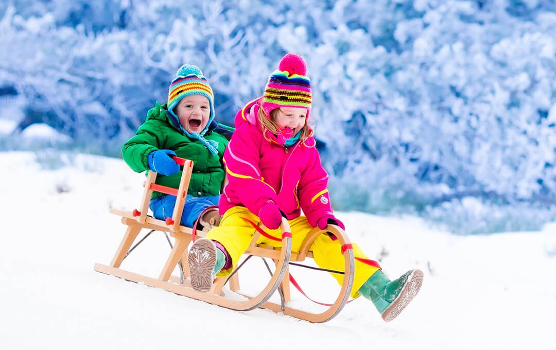 A close-up of two children wearing winter clothing riding a sleigh down a snowy slope.