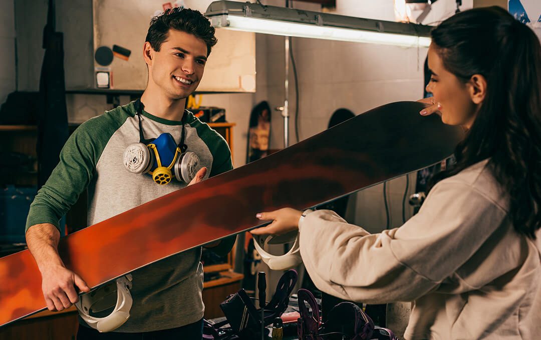 A close-up of a young man giving a snowboard to a girl client after a maintenance repair.