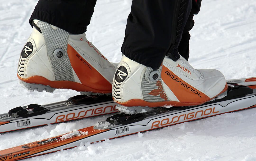 A close-up of a man wearing ski boots standing on a ski blade on snow.